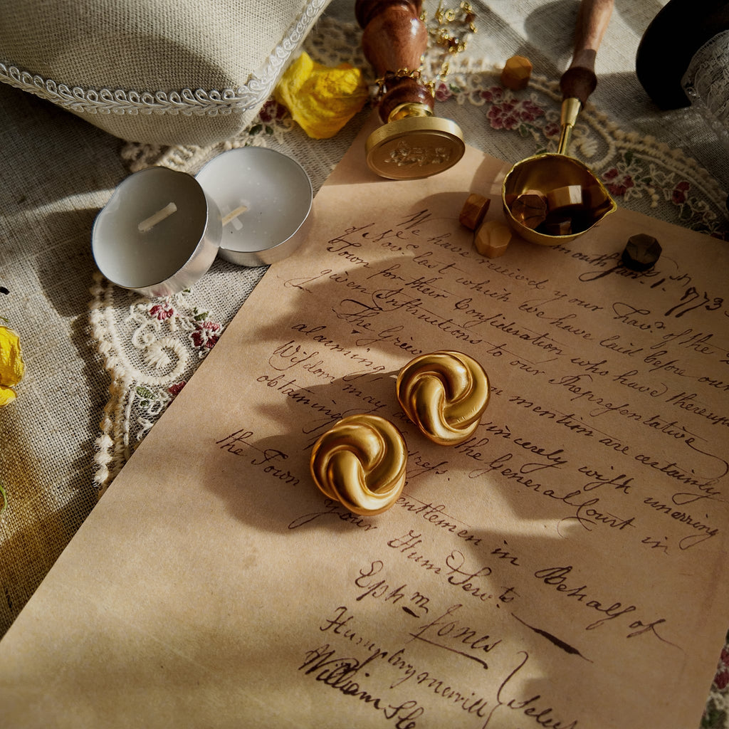 A detailed view of the matching Anne Klein knot earrings, echoing the bracelet's design with a bold, confident circle of warm, brushed matte gold.