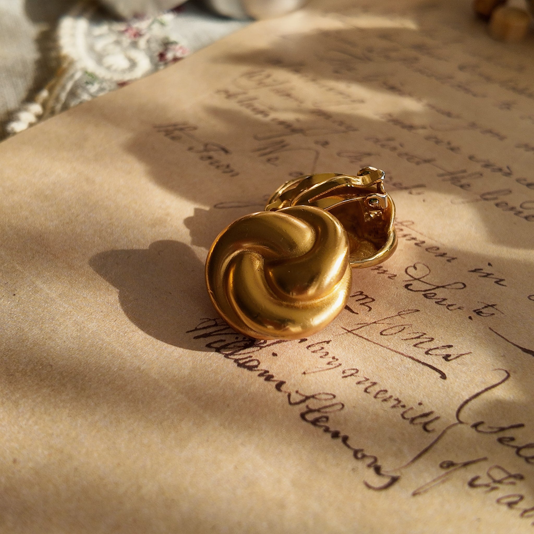 A detailed view of the matching Anne Klein knot earrings, echoing the bracelet's design with a bold, confident circle of warm, brushed matte gold.