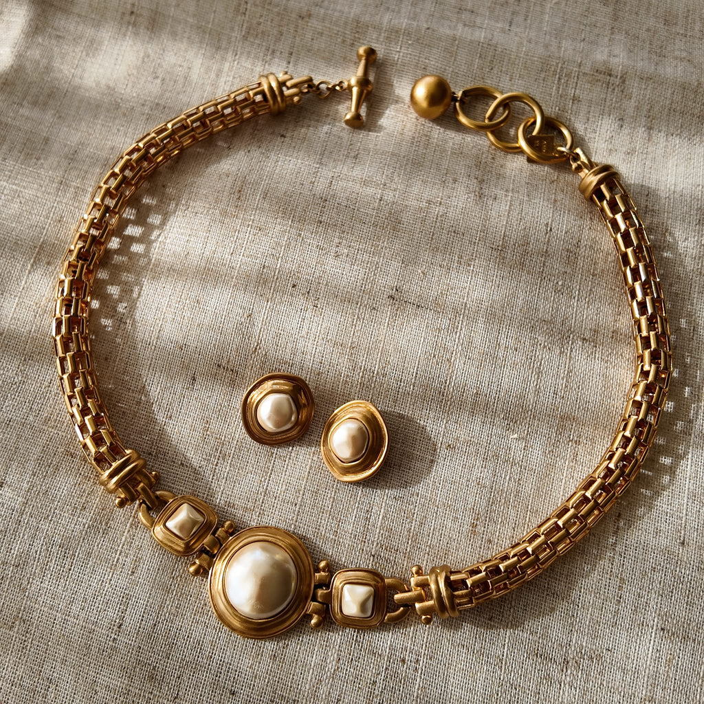 The "A Seat at the Table" vintage Anne Klein jewelry set, showcasing a substantial matte gold plait necklace with baroque pearls and matching clip-on earrings.