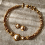 The "A Seat at the Table" vintage Anne Klein jewelry set, showcasing a substantial matte gold plait necklace with baroque pearls and matching clip-on earrings.