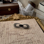 The "There is a Crack in Everything" brooch, an antique Gothic filigree bow design in a faded, antiqued silver finish with a central black glass pane.