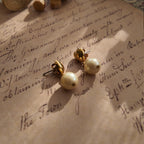 An angled view of the gold dangle earrings, highlighting the playful movement of the luminous pearl suspended below the polished heart stud.