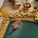 An angled view of the red enamel flower earrings, highlighting the immaculate, pearlescent finish of the enamel and the bright, sparkling central rhinestone.