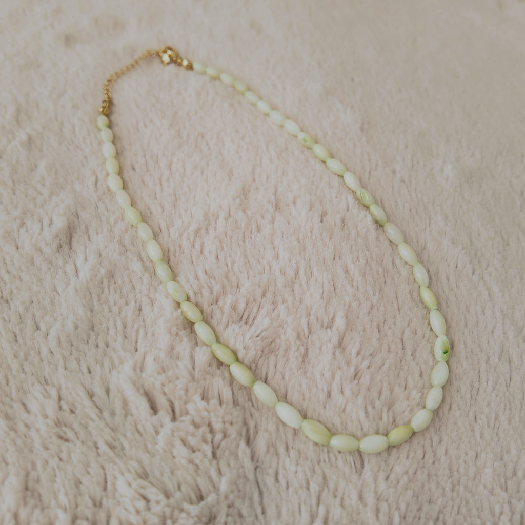 The "Nature Child" shell necklace styled on a piece of driftwood to emphasize its "Beachcomber Chic" and organic aesthetic, a true piece of the ocean.