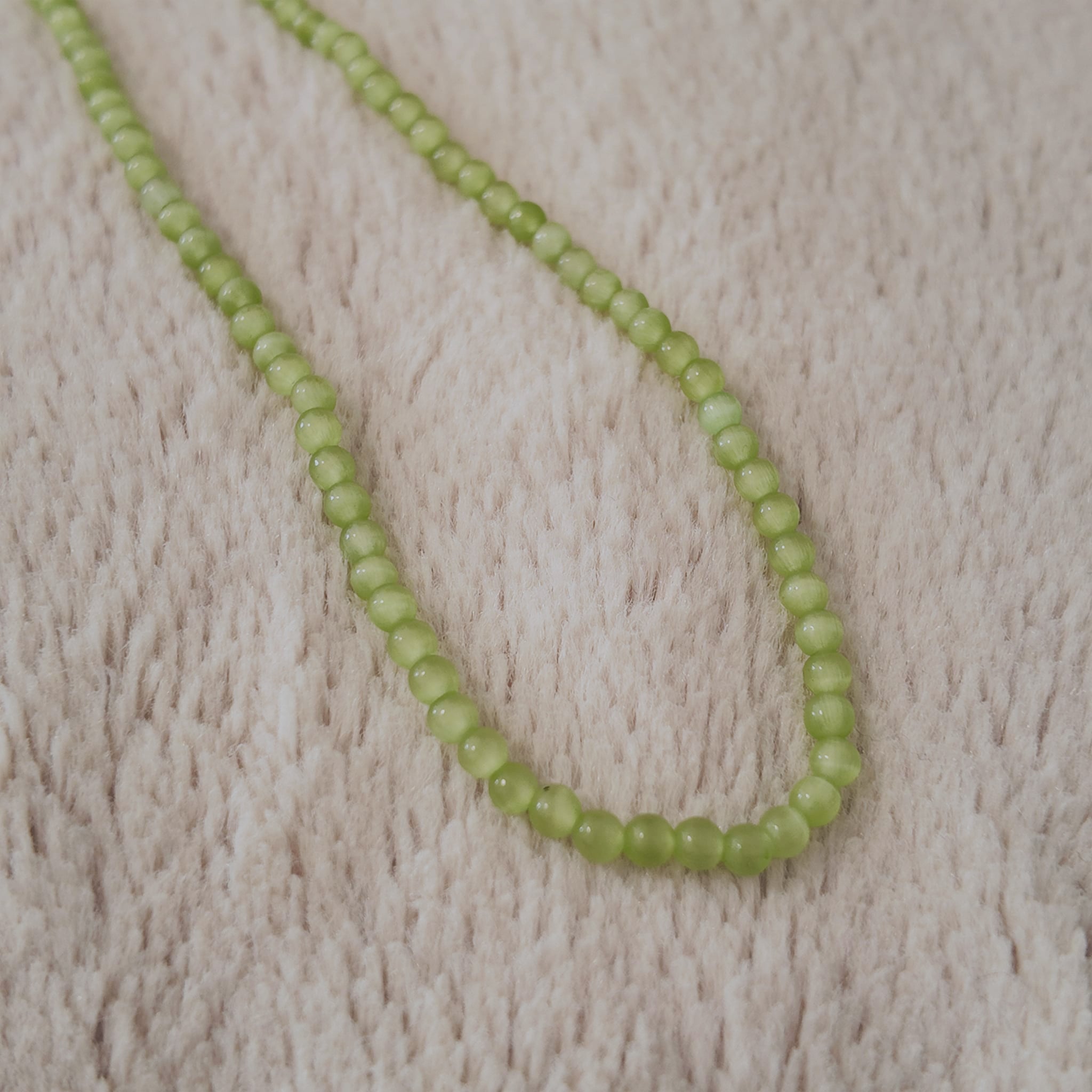 The "Emerald Spark" choker styled as a layering necklace with a gold chain, demonstrating its versatility and its ability to add a spark of vibrant color.