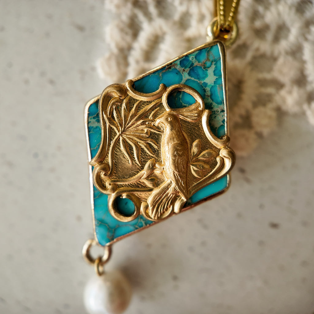 The "Garden of Good News" Chinoiserie chic necklace, featuring a large turquoise-hued stone pendant with a vintage brass magpie and a dangling freshwater pearl.