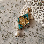 The "Garden of Good News" Chinoiserie chic necklace, featuring a large turquoise-hued stone pendant with a vintage brass magpie and a dangling freshwater pearl.