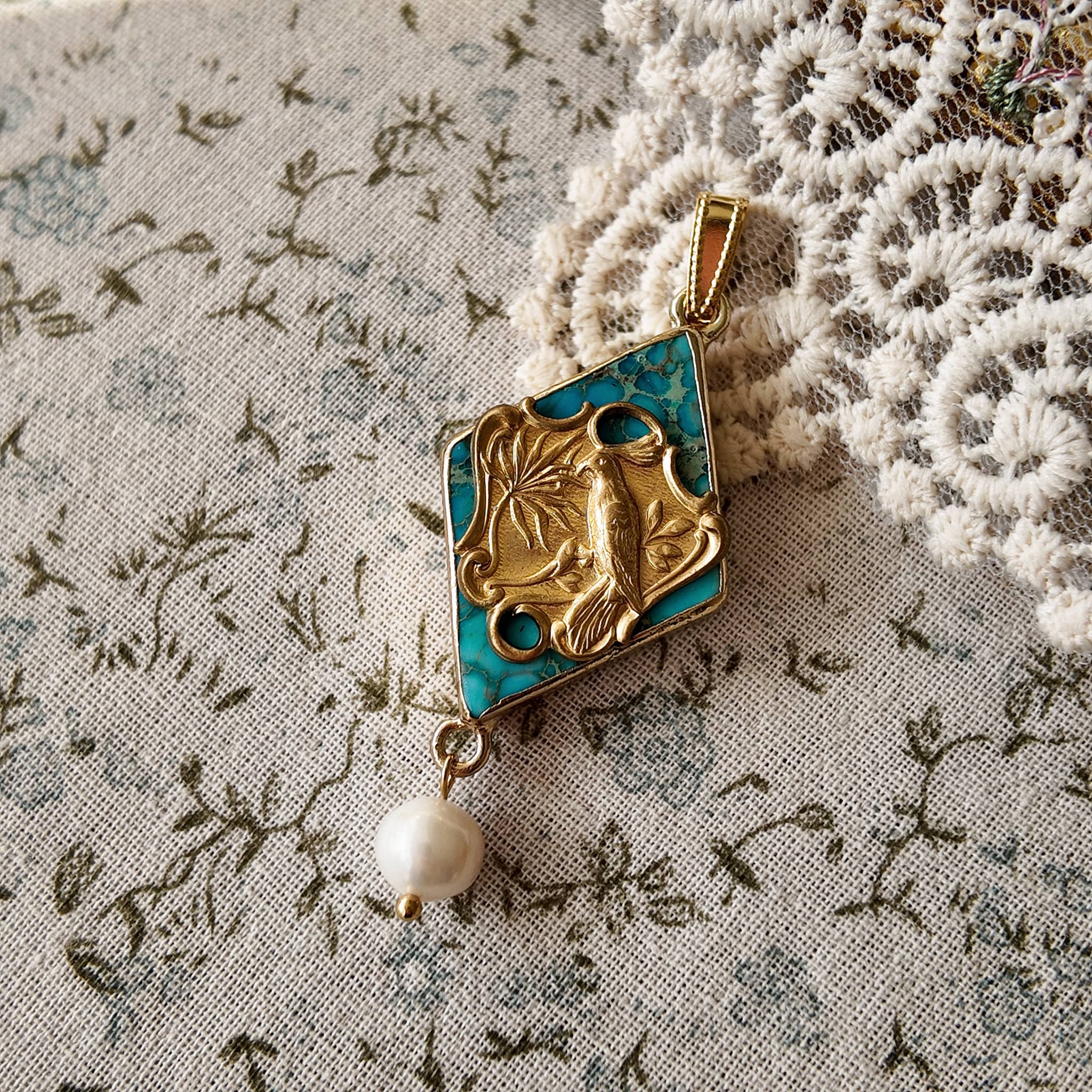 The "Garden of Good News" Chinoiserie chic necklace, featuring a large turquoise-hued stone pendant with a vintage brass magpie and a dangling freshwater pearl.