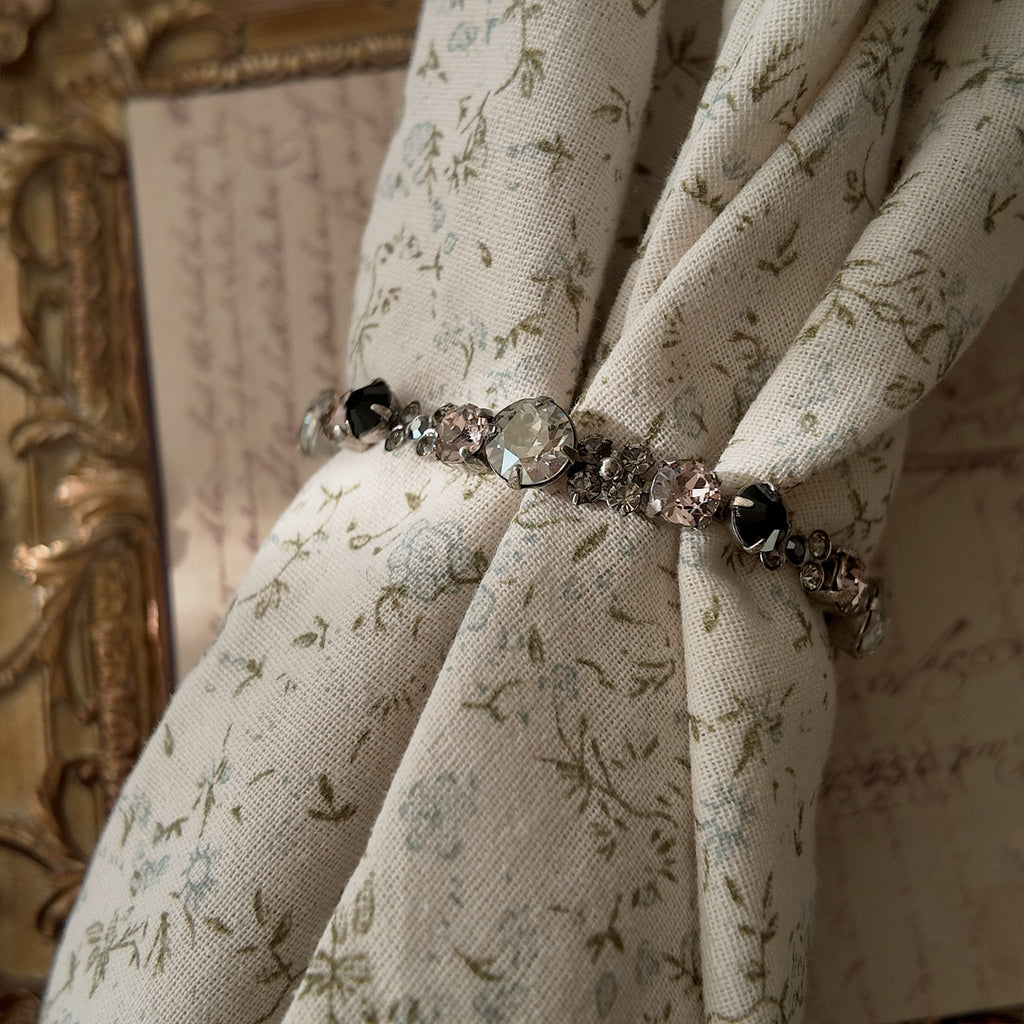 A dainty Sorrelli crystal bracelet worn on a wrist, showcasing its delicate size and its "sweet and sinister" pink and black color palette, perfect for Coquette style.