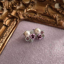 The "Winter Rose," a pair of exquisite, dainty vintage stud earrings, featuring a central pearl surrounded by pink and clear crystals and a tiny purple rose.