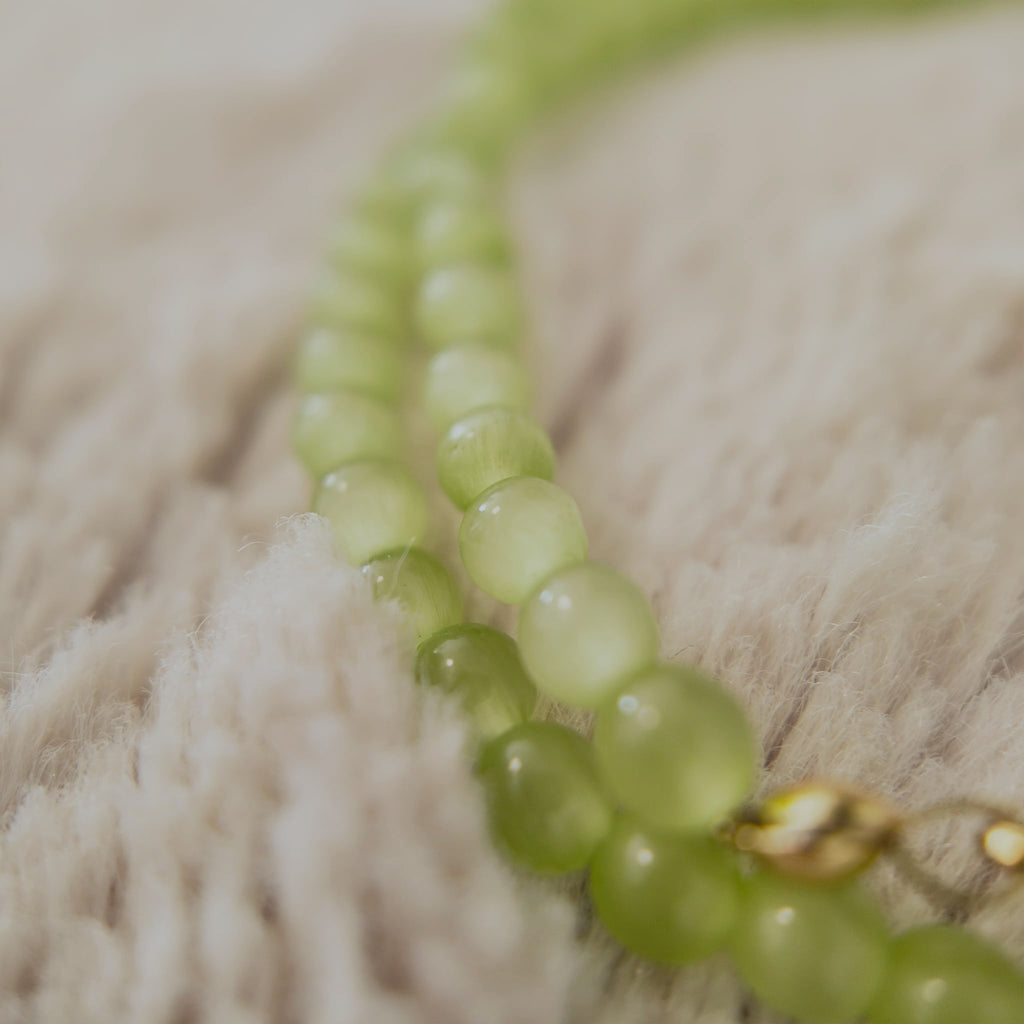 The "Emerald Spark," a dainty, artisan-made beaded choker necklace, strung with petite, micro-round Green Cat's Eye stone beads.