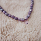 The "Twilight Tear," an ethereal, artisan-made beaded necklace, featuring faceted purple fire agate beads and a central, natural amethyst teardrop pendant.
