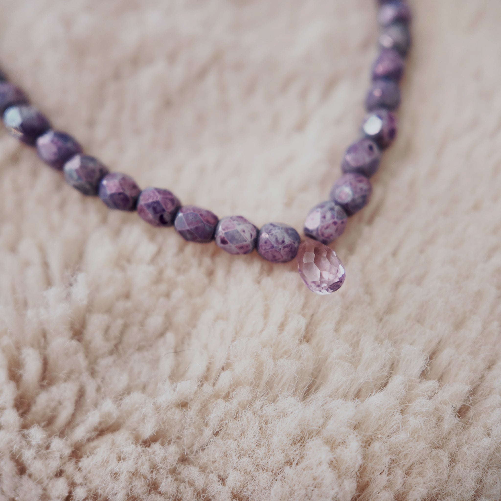 The "Twilight Tear," an ethereal, artisan-made beaded necklace, featuring faceted purple fire agate beads and a central, natural amethyst teardrop pendant.