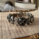 An angled view of "The Forbidden Scholar" Gothic bracelet, highlighting the intricate, lace-like metal filigree layered over the large, obsidian-like stones.