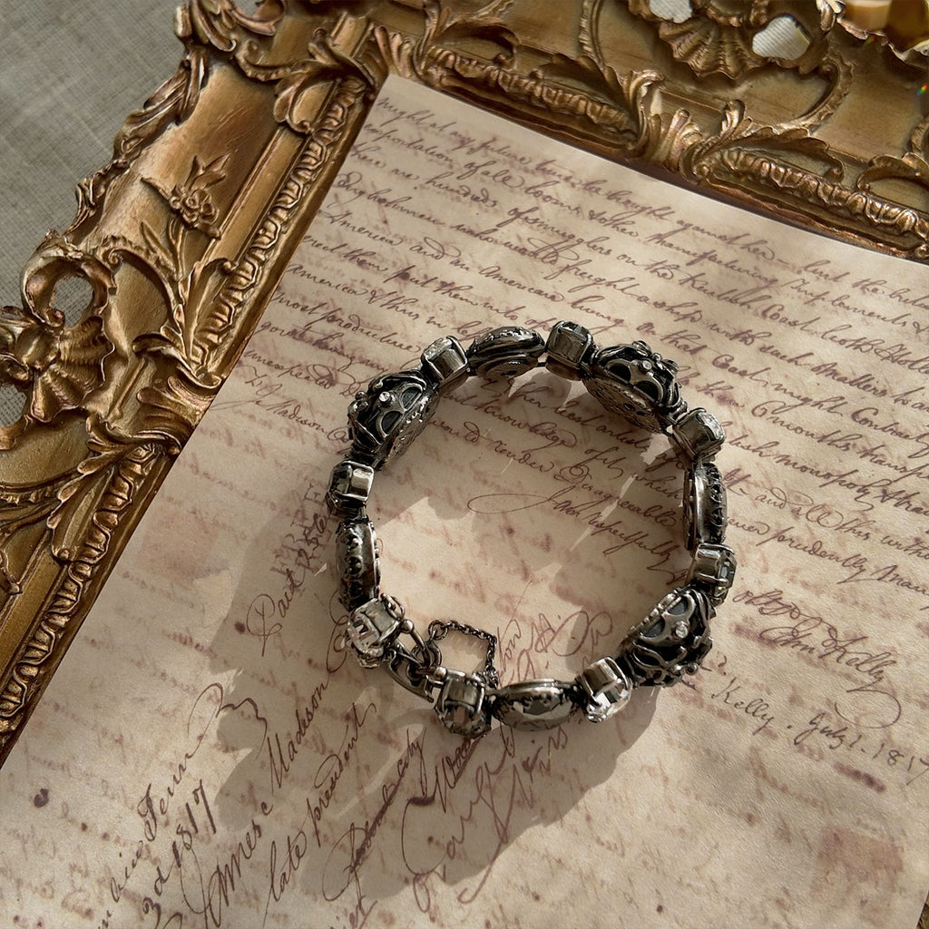 An angled view of "The Forbidden Scholar" Gothic bracelet, highlighting the intricate, lace-like metal filigree layered over the large, obsidian-like stones.