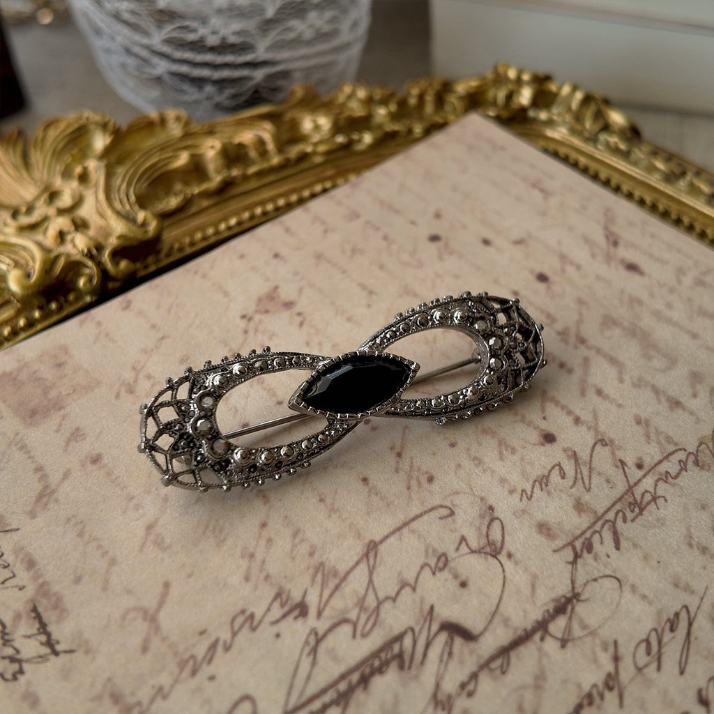 An angled view of the antique bow brooch, highlighting the intricate, web-like silver filigree that demonstrates its historical craftsmanship, despite its flaws.