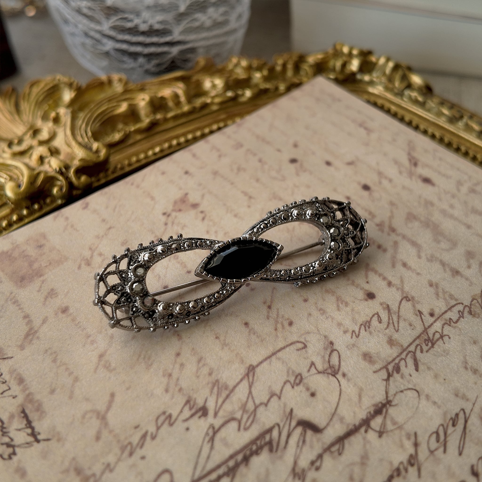 An angled view of the antique bow brooch, highlighting the intricate, web-like silver filigree that demonstrates its historical craftsmanship, despite its flaws.