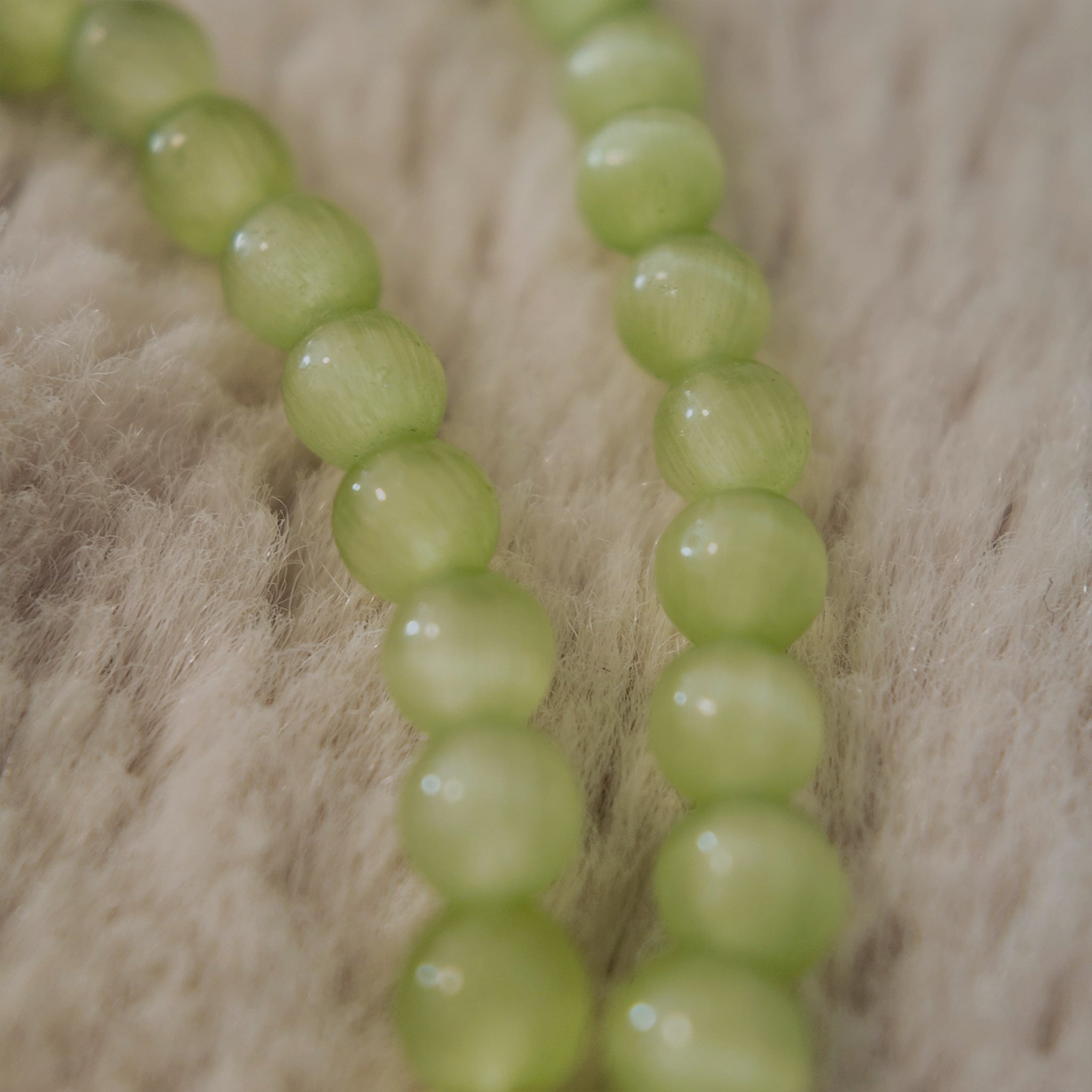 A macro shot detailing the magical "Cat's Eye" effect, a band of reflected light known as chatoyancy that moves across the surface of each green bead.