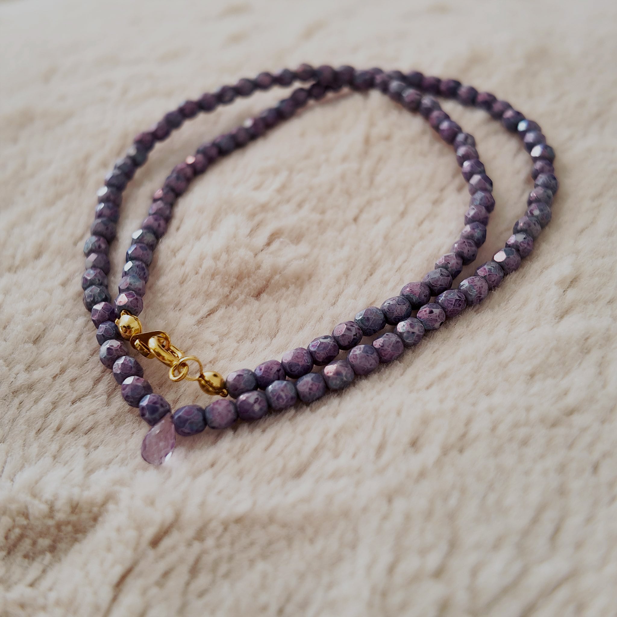 An angled view of the handmade necklace, highlighting the stunning, iridescent "aura" sheen that shifts between blue and pink on the purple fire agate beads.