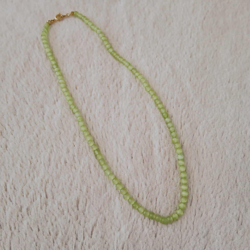 The "Emerald Spark" Cat's Eye necklace styled on a large green leaf to emphasize its "Jungle Vibes" and its identity as a spark of natural vitality.