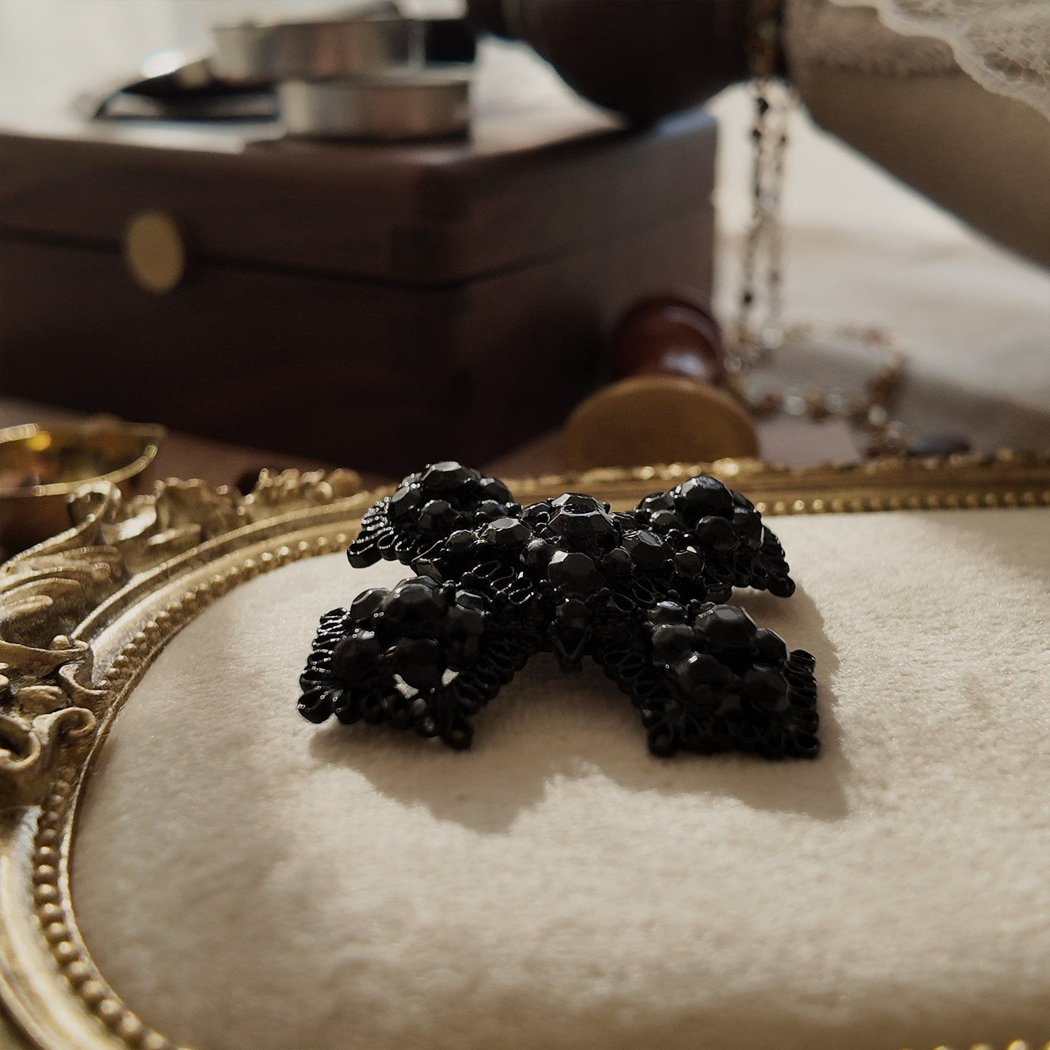 An angled view of "The Vampire Matriarch" brooch, highlighting the three-dimensional depth of the black-painted metal filigree and the deep-set crystals.