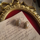 The "Maiden's Shield" earrings styled on a book of poetry to emphasize their "rebellious heart" aesthetic and their connection to the spirited, outspoken heroines of Victorian novels.