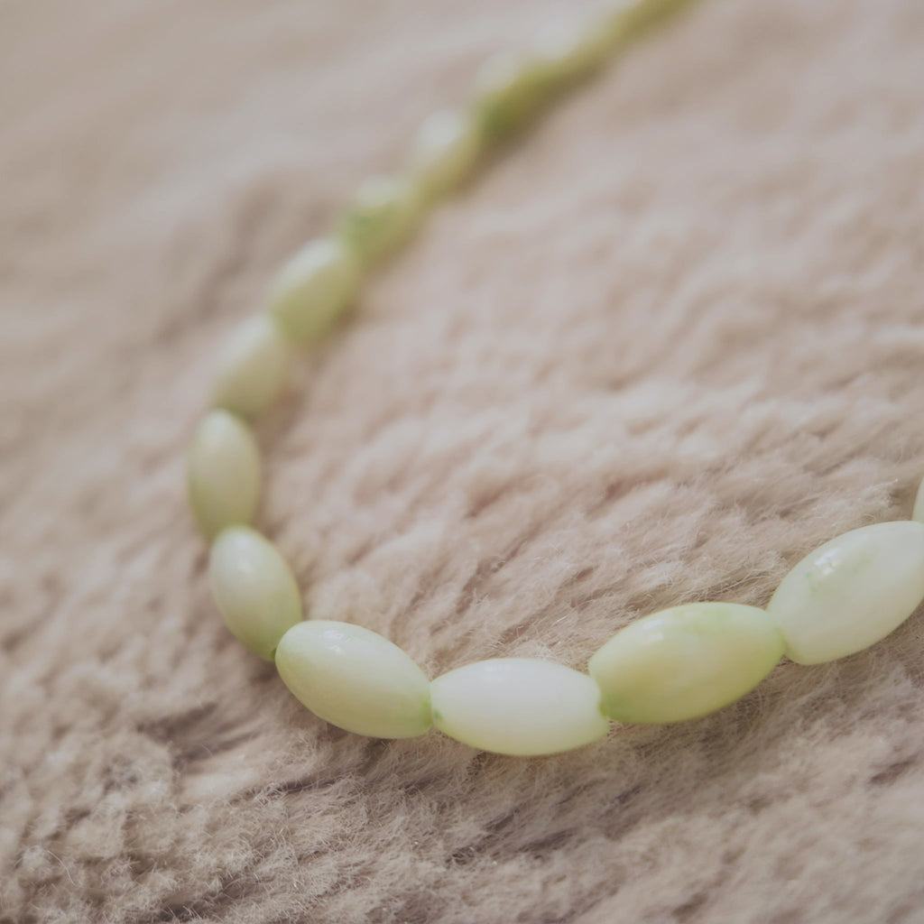 The "Nature Child," an artisan-made beaded choker necklace, featuring natural shell beads in a soft, interwoven pattern of mint green and white.