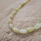 The "Nature Child," an artisan-made beaded choker necklace, featuring natural shell beads in a soft, interwoven pattern of mint green and white.