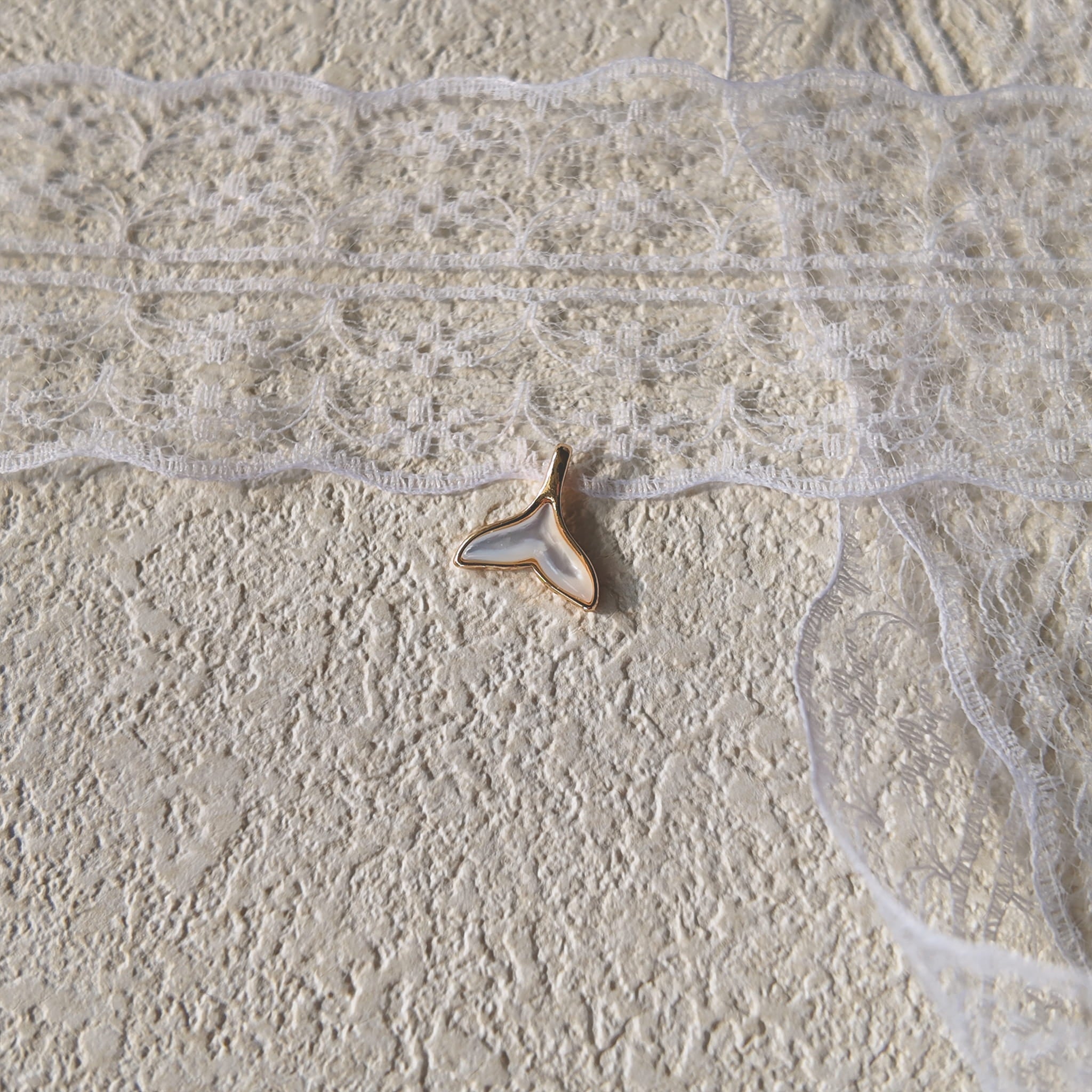 The "Siren's Farewell" mermaid tail charm worn on a fine gold chain, showcasing its delicate, feather-light size and its ethereal, minimalist aesthetic.