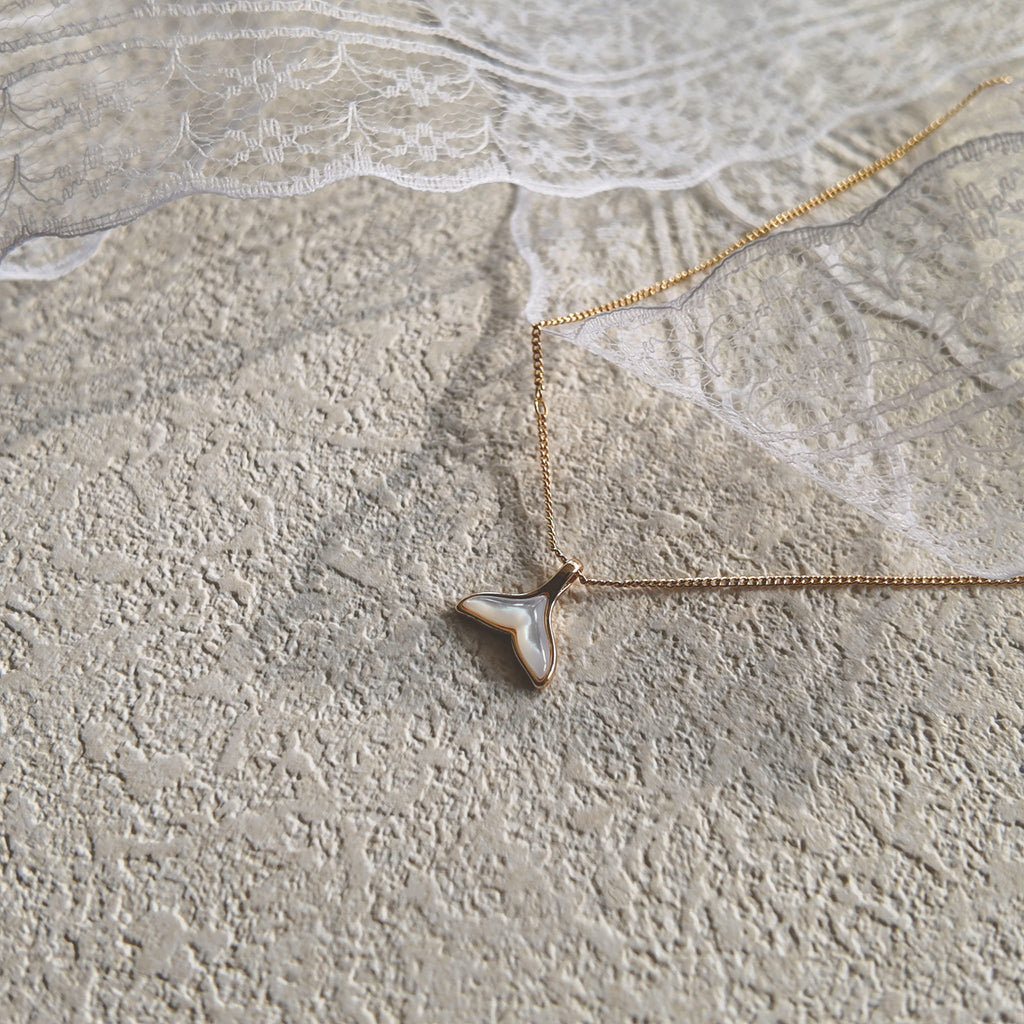 The "Siren's Farewell" mermaid tail charm worn on a fine gold chain, showcasing its delicate, feather-light size and its ethereal, minimalist aesthetic.