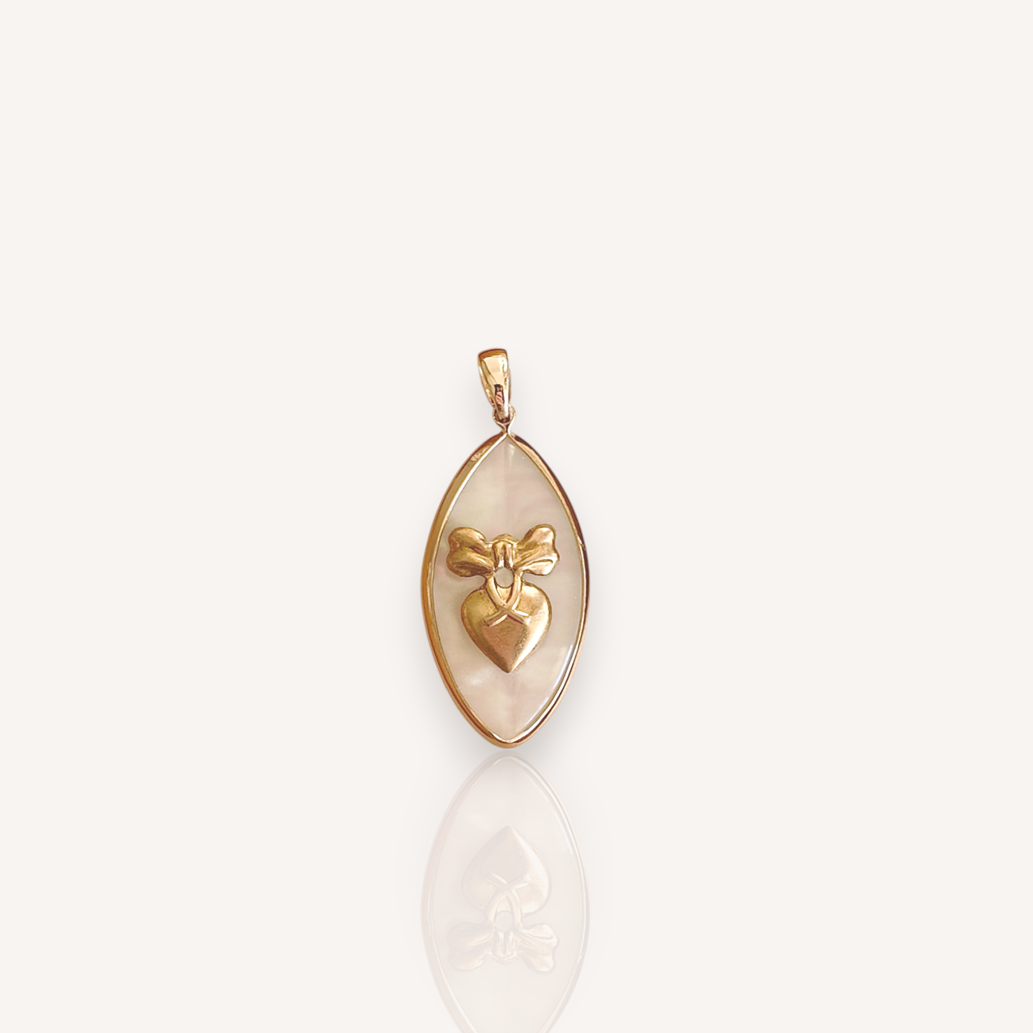  Front view of The Pearl Bow pendant featuring a marquise Mother-of-Pearl with a vintage brass bow and dangling heart charm.