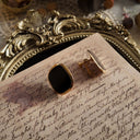 An angled view of the geometric earrings, highlighting the clean lines, the glossy finish of the black resin, and the lustrous sheen of the gold plating.