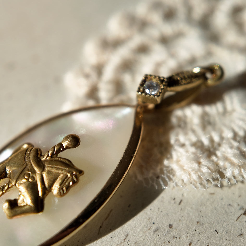 An angled view of the "Ticket to Dreamland" artisan pendant, highlighting the layered construction of the upcycled vintage brass horse and MOP components.