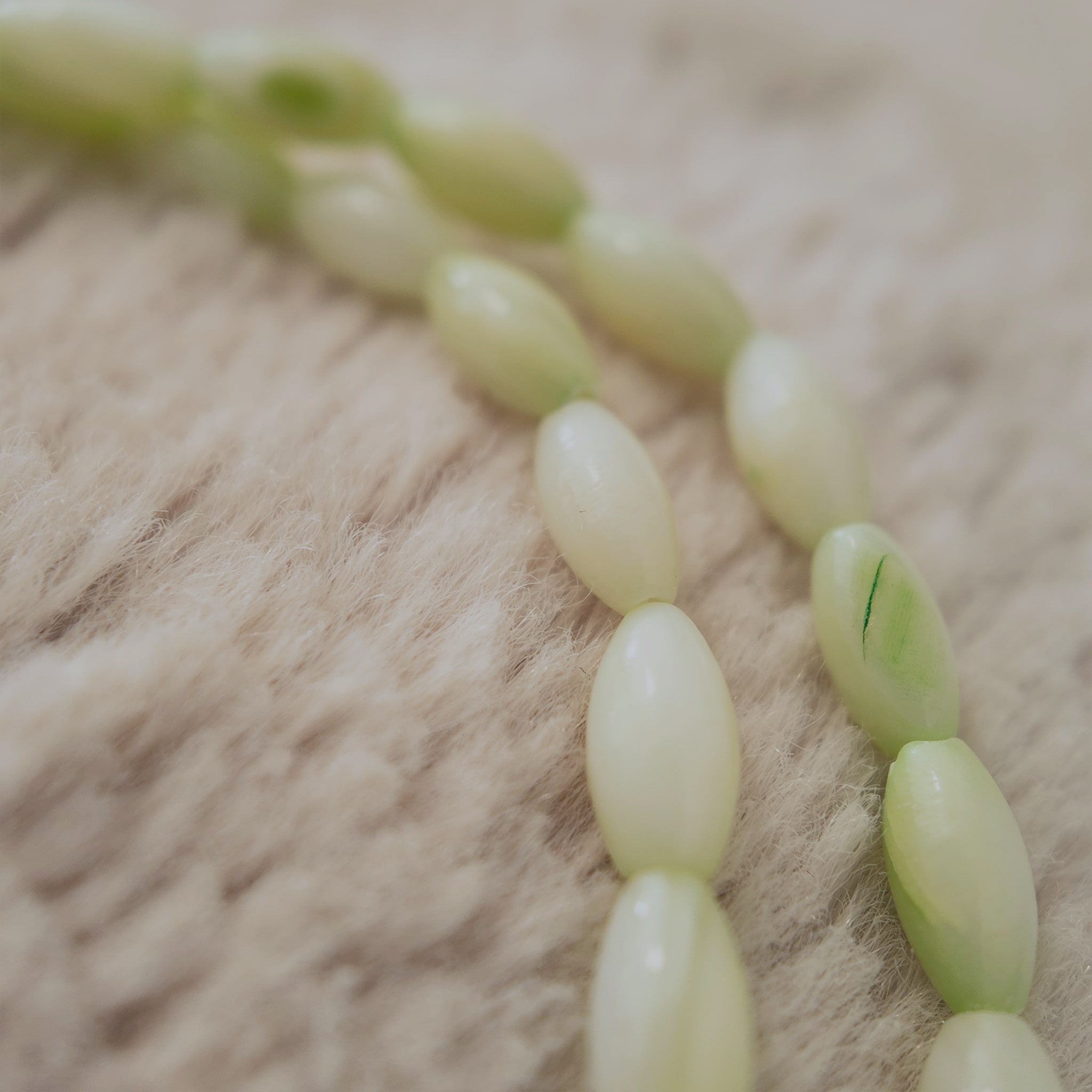 A macro shot detailing the sleek, tapered shuttle shape of the natural shell beads and the unique, soft blend of milky white and mint green colors.