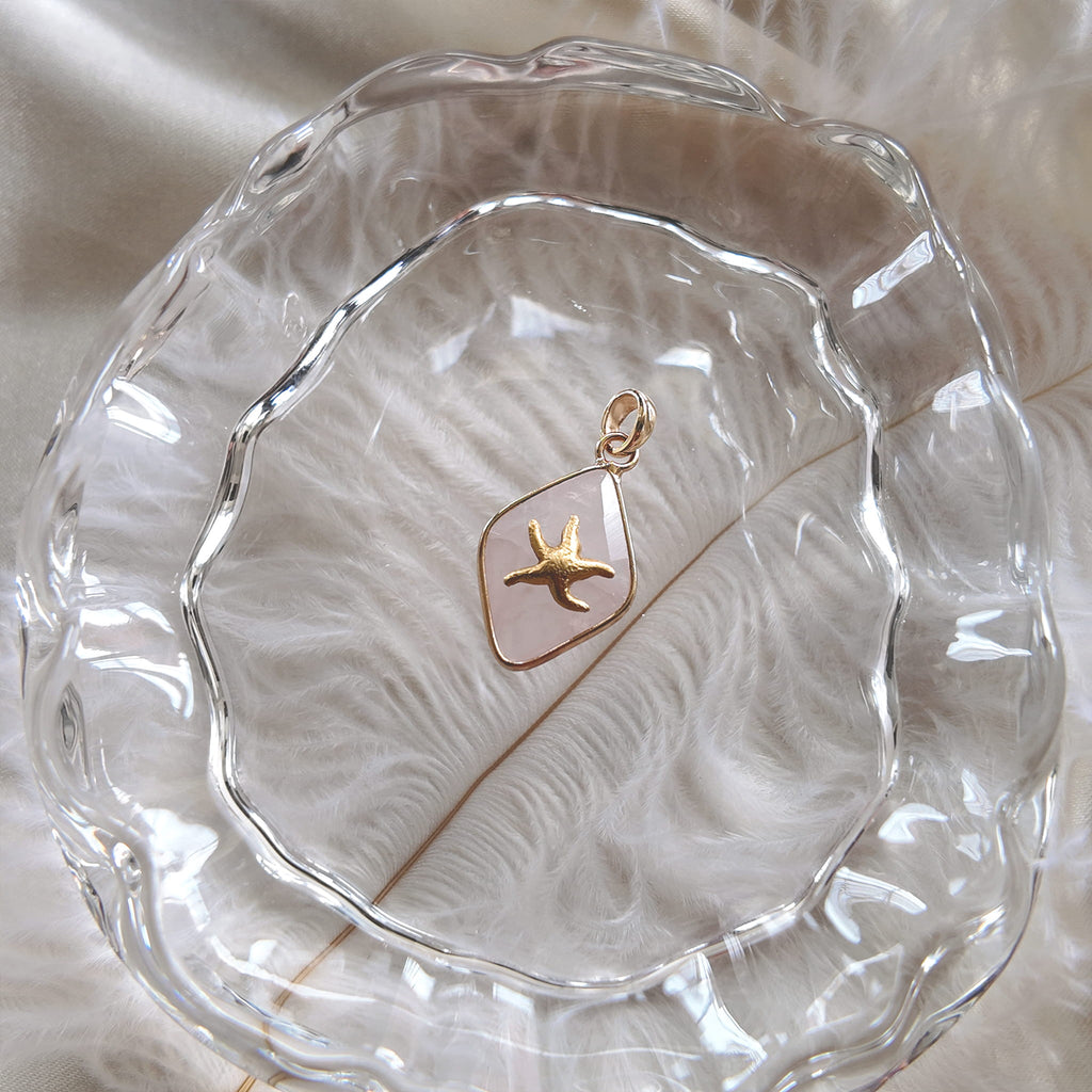 The handmade White Quartz starfish charm styled on a piece of sea-worn wood to emphasize its connection to oceanic resilience and its identity as a perfect, meaningful gift.