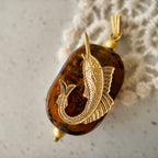 The "Leaping Wanderer" oceanic necklace from The Character Arc, featuring a rectangular amber art glass charm with a vintage brass tuna fish.