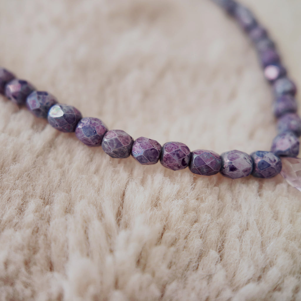 A macro shot detailing the meticulously faceted purple fire agate and the clear, polished quality of the natural amethyst teardrop at the center.