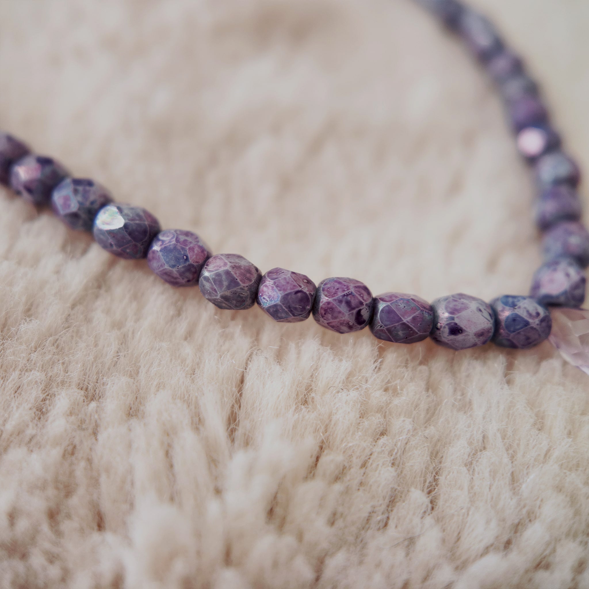 A macro shot detailing the meticulously faceted purple fire agate and the clear, polished quality of the natural amethyst teardrop at the center.