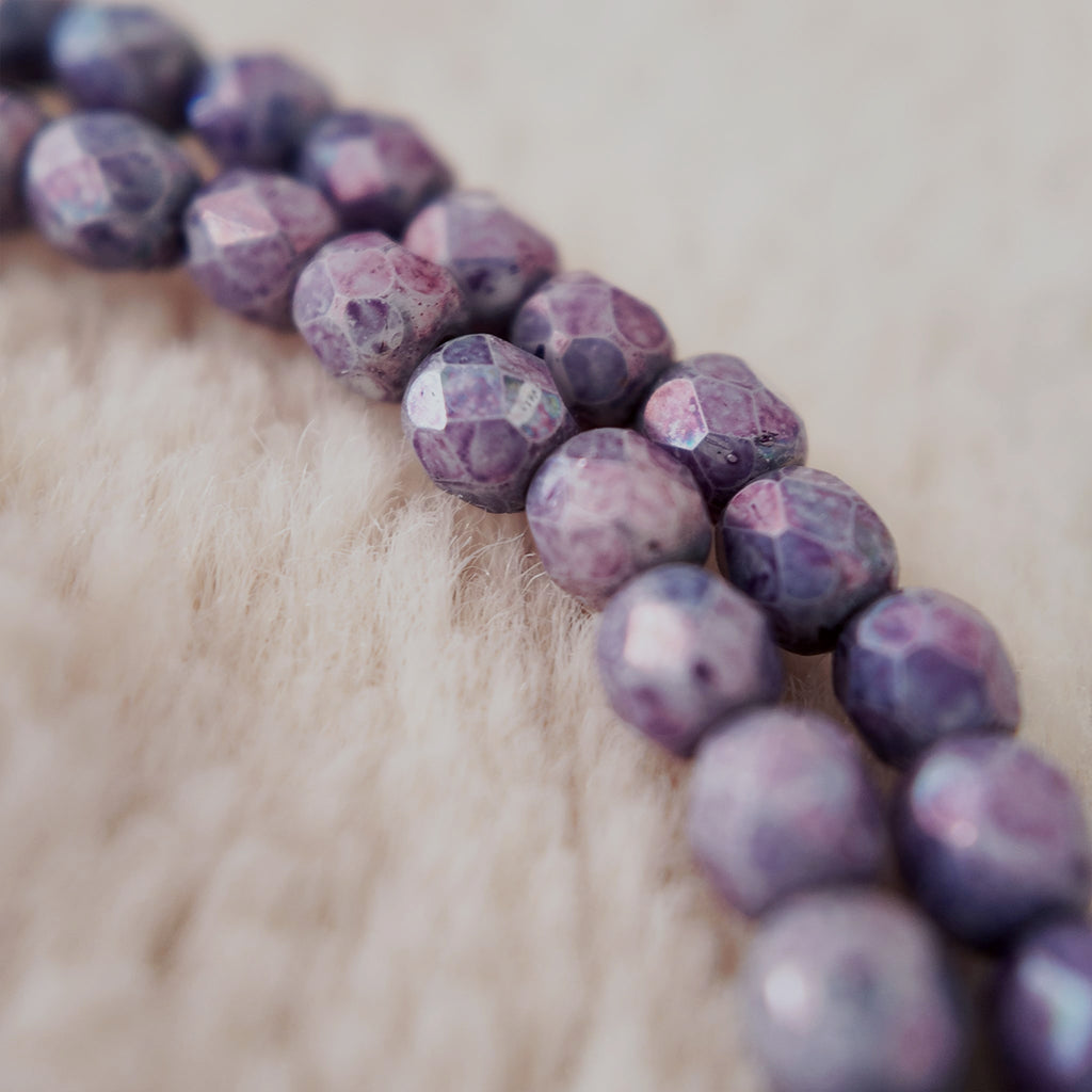 A macro shot detailing the meticulously faceted purple fire agate and the clear, polished quality of the natural amethyst teardrop at the center.