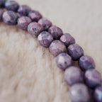 A macro shot detailing the meticulously faceted purple fire agate and the clear, polished quality of the natural amethyst teardrop at the center.