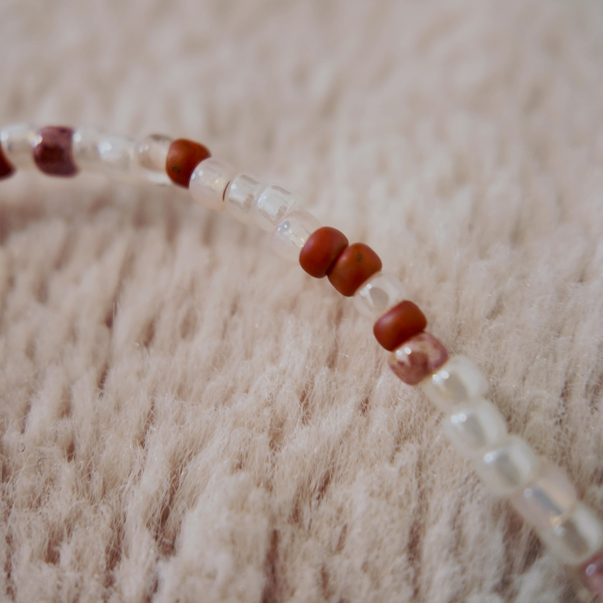 A macro shot detailing the thoughtful mix of opaque and translucent glass seed beads and the clean, bold lines of the red Heart-Cross pendant