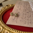 A macro shot detailing the intricate, lace-like filigree work and the sparkling, hand-set quality of the tiny green crystal rhinestones on these vintage earrings.
