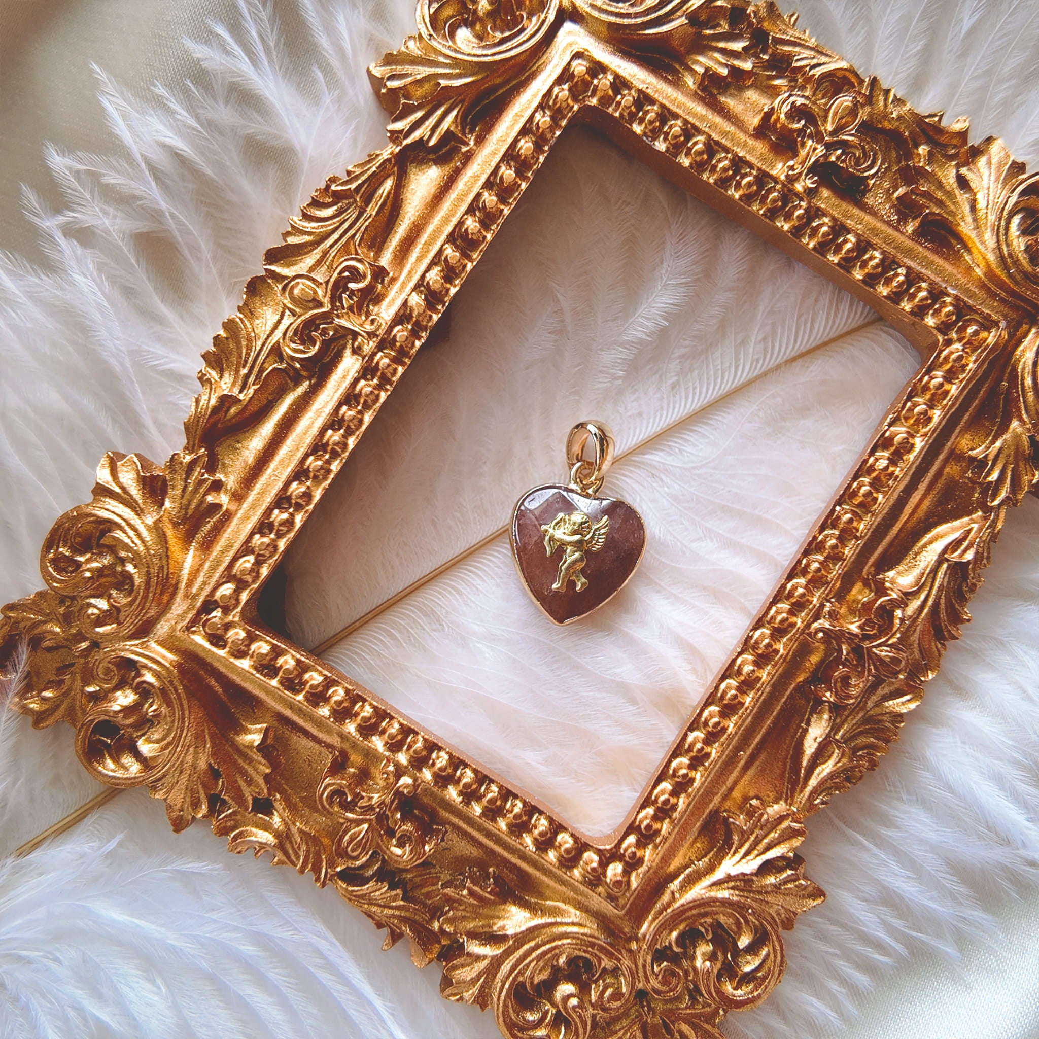 The handmade Strawberry Quartz Cupid charm styled on a piece of pink silk to emphasize its connection to romance and its identity as a perfect, sweet gift.