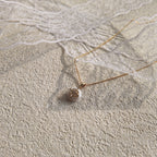 A woman wearing the "Mermaid's Tear" pearl charm, showcasing its delicate size and its identity as a piece of sacred, romantic jewelry.