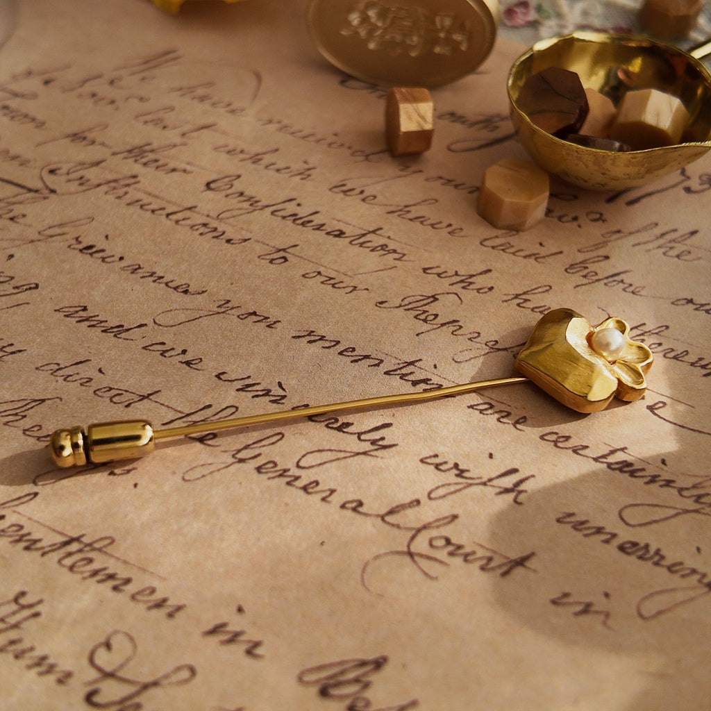 An angled view of the matte gold heart brooch, highlighting its smooth, non-reflective surface and the gentle sheen of the crowning pearl.