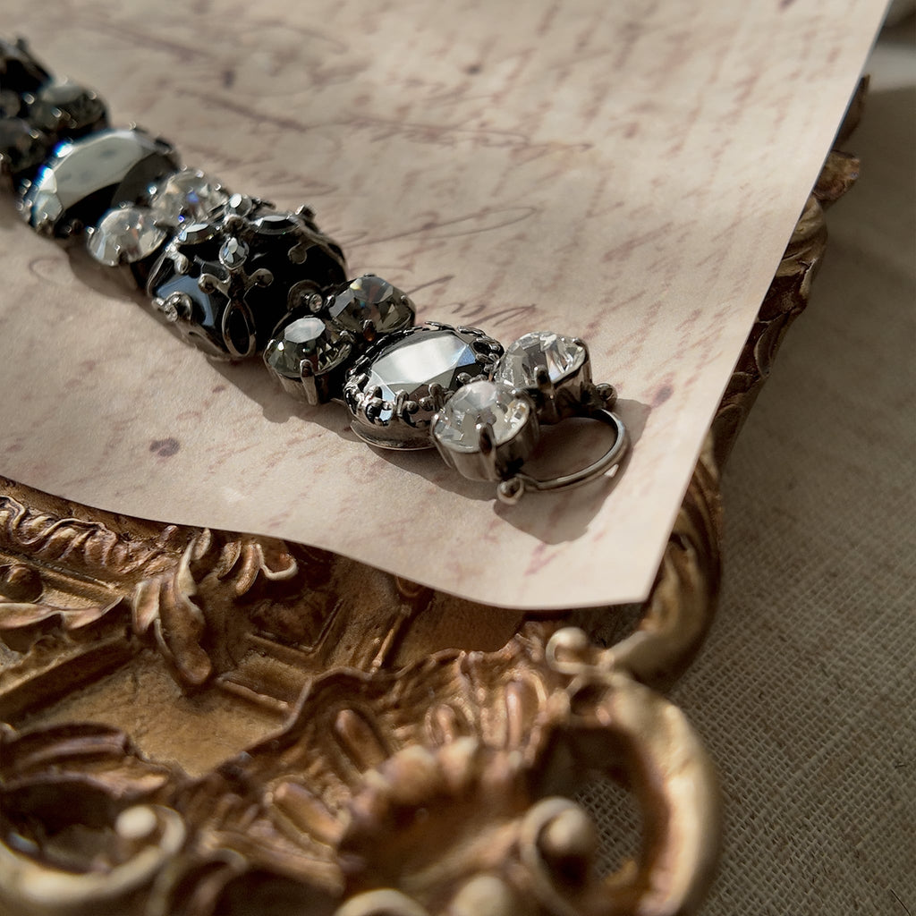 A macro shot detailing the brilliant sparkle of the black diamond crystals and the "poetic decay" of the antiqued filigree on this collectible Sorrelli bracelet.