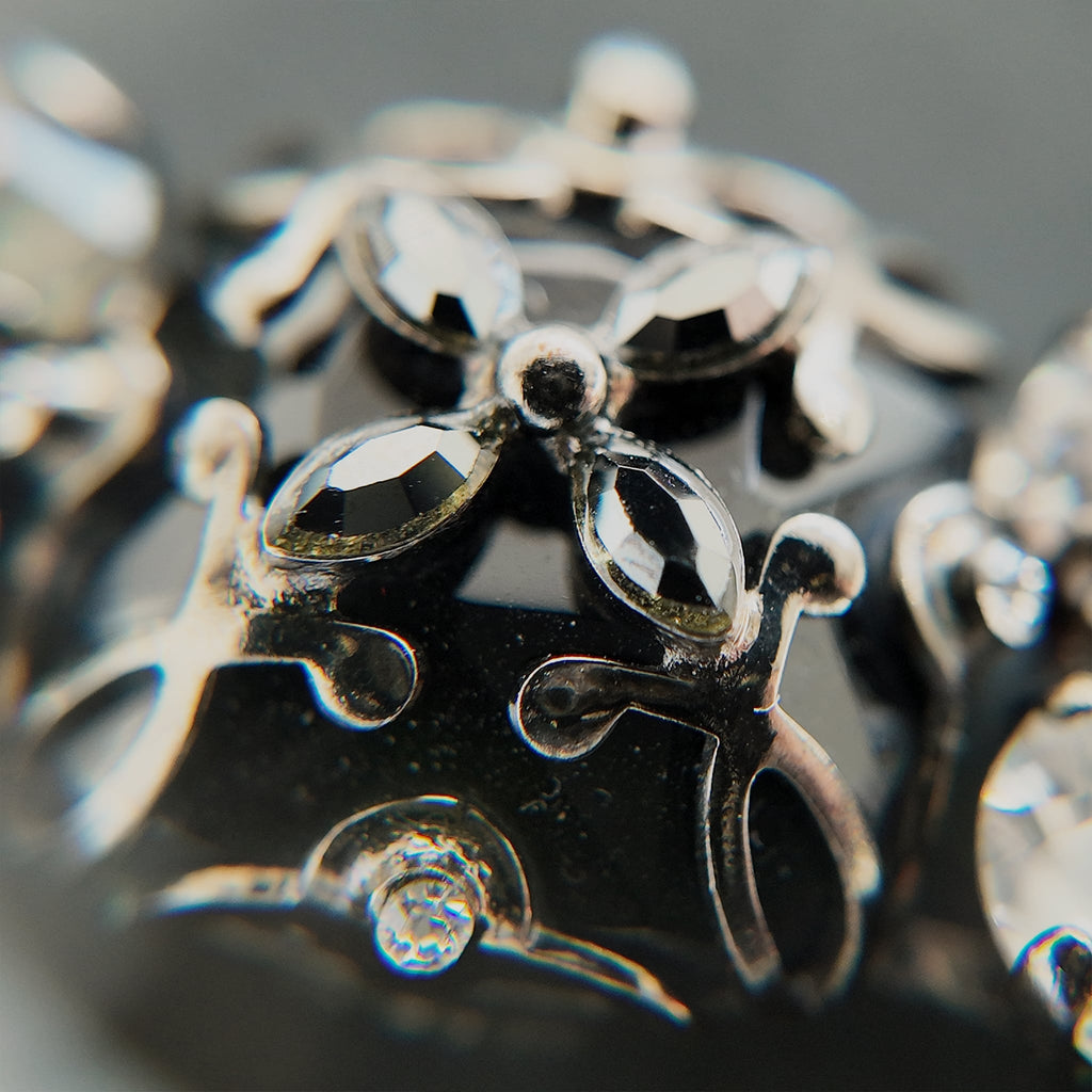 A macro shot detailing the brilliant sparkle of the black diamond crystals and the "poetic decay" of the antiqued filigree on this collectible Sorrelli bracelet.