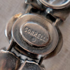 A close-up of the authentic "Sorrelli" signature hang tag on the back of the antiqued silver-tone vintage statement bracelet.