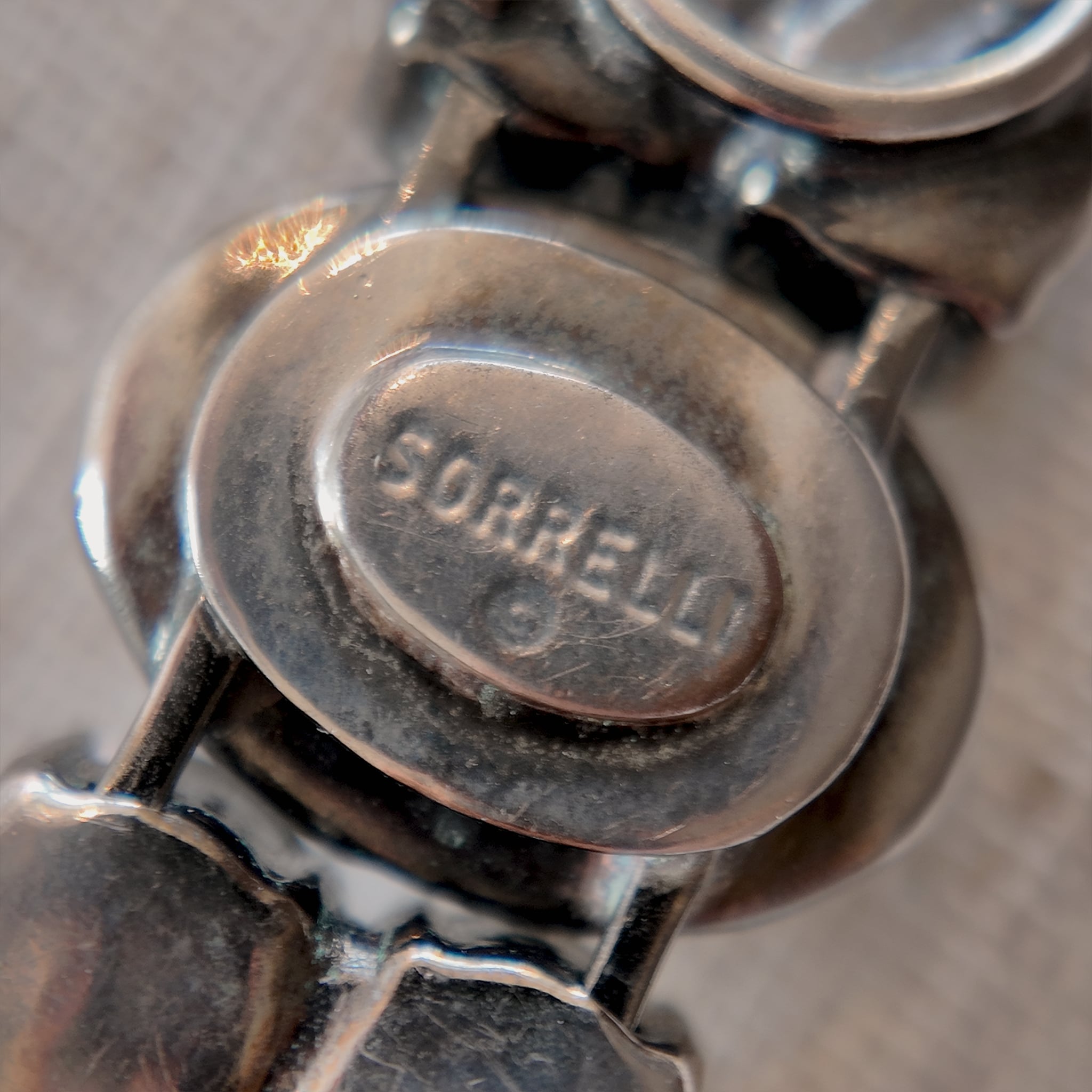 A close-up of the authentic "Sorrelli" signature hang tag on the back of the antiqued silver-tone vintage statement bracelet.