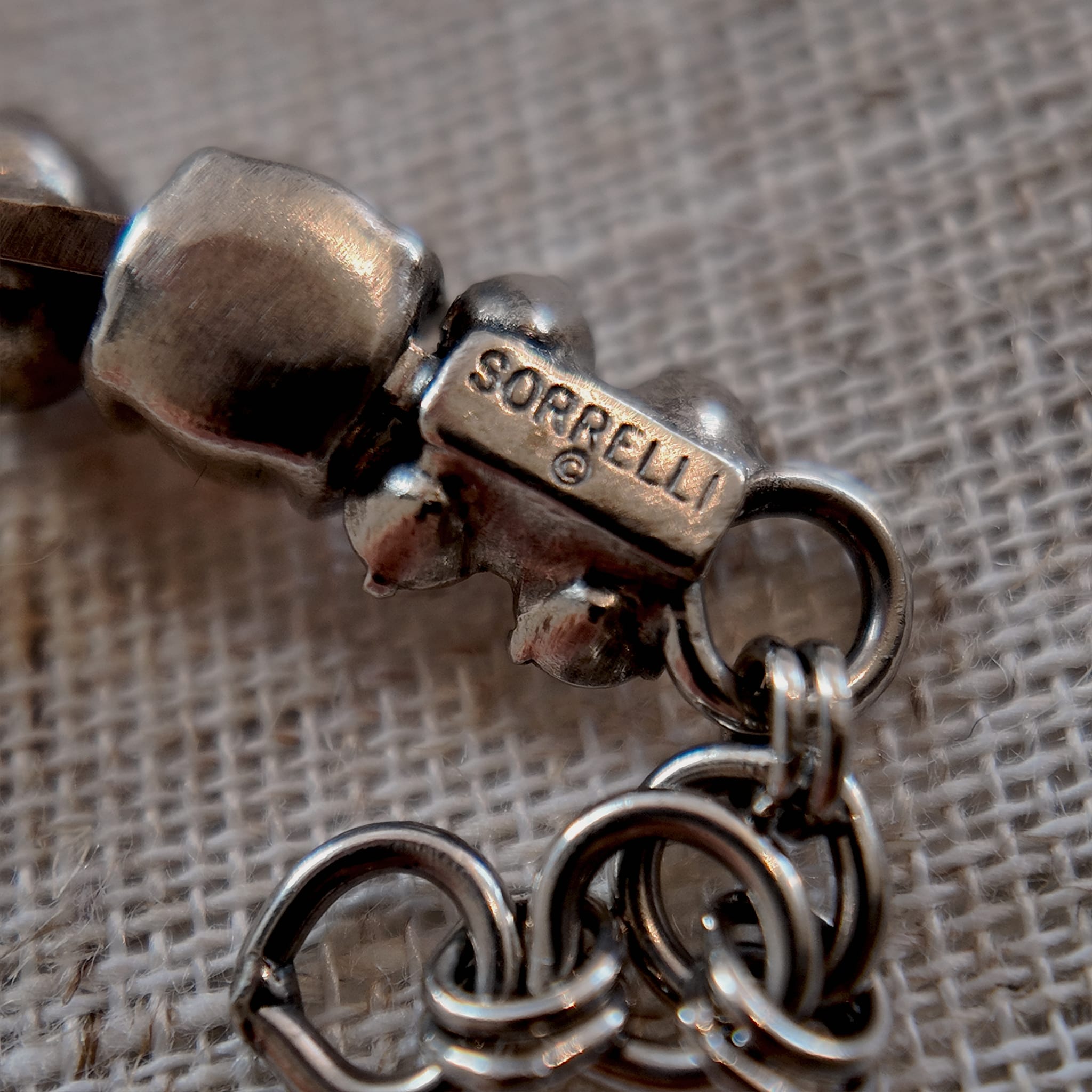A close-up of the authentic "Sorrelli" signature hang tag on the back of the vintage pink and black crystal bracelet.
